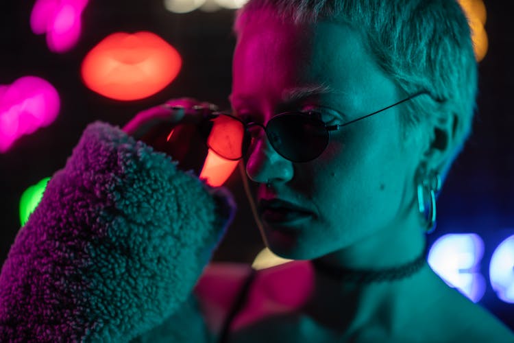 A Woman Wearing Sunglasses Standing Near The Neon Lights