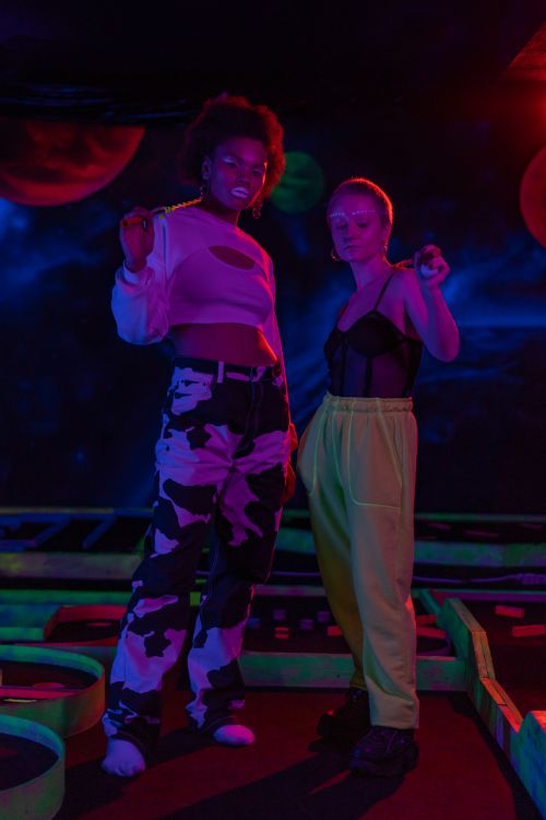 Free Two stylish women pose confidently under neon lights in a vibrant club room setting. Stock Photo