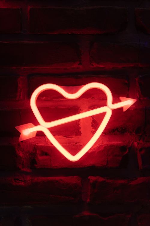 Free Bright neon heart with arrow sign on a rustic brick wall, creating a romantic and bold ambiance. Stock Photo