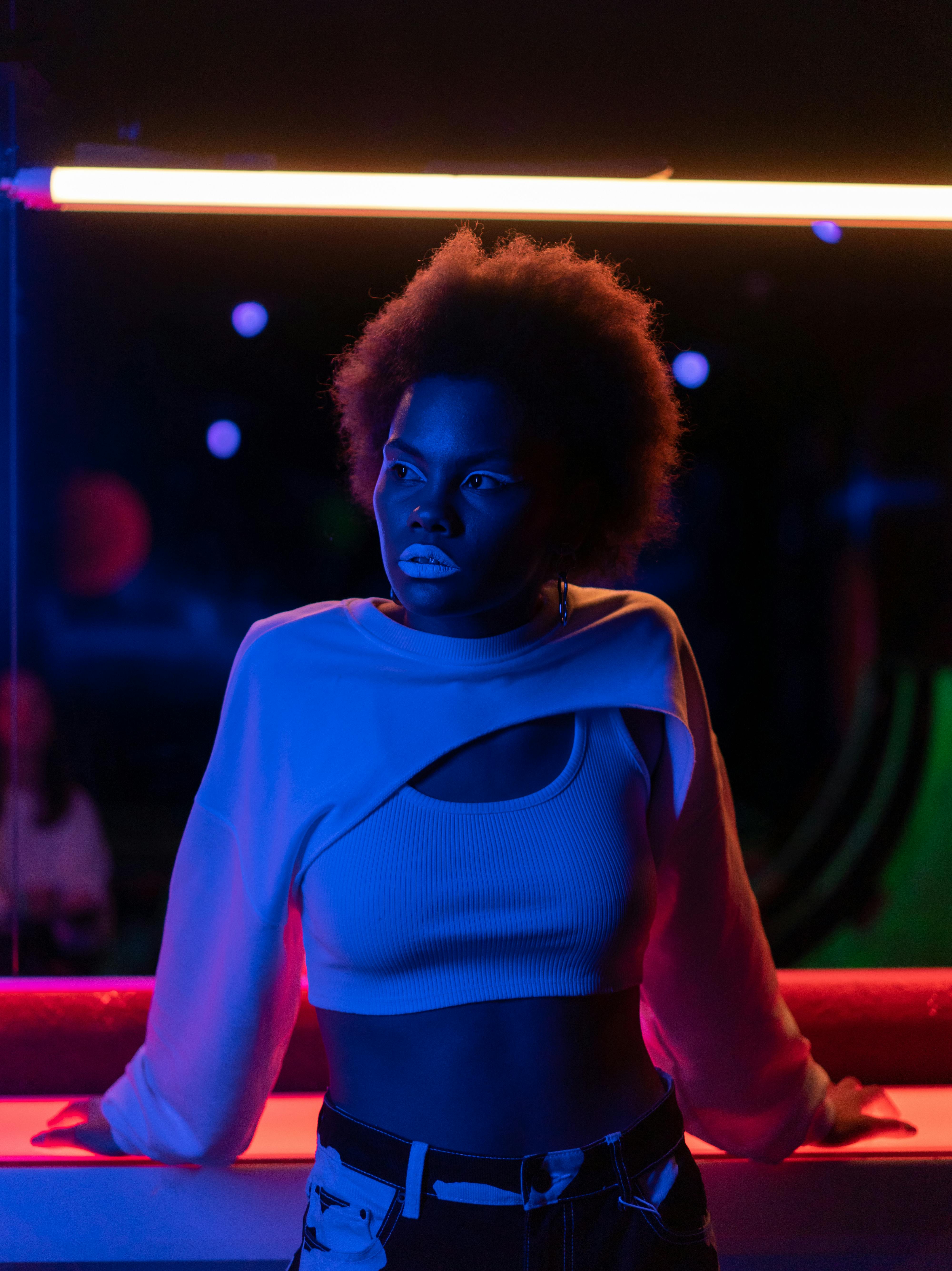 A fashionable woman poses under striking neon lights, showcasing modern style and vibrant colors.