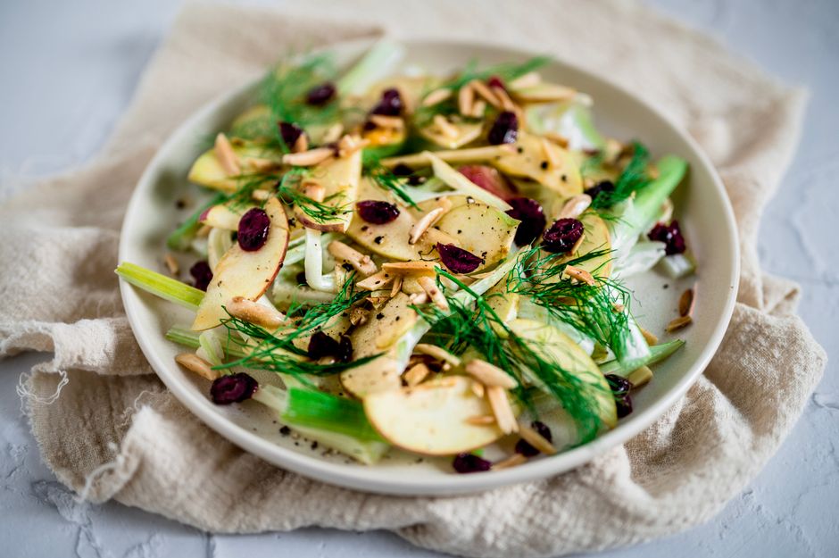 A platter of sliced pink-fleshed cara cara oranges layered with shaved fennel, avocado, arugula, red onion, and torn mint, drizzled with olive oil.