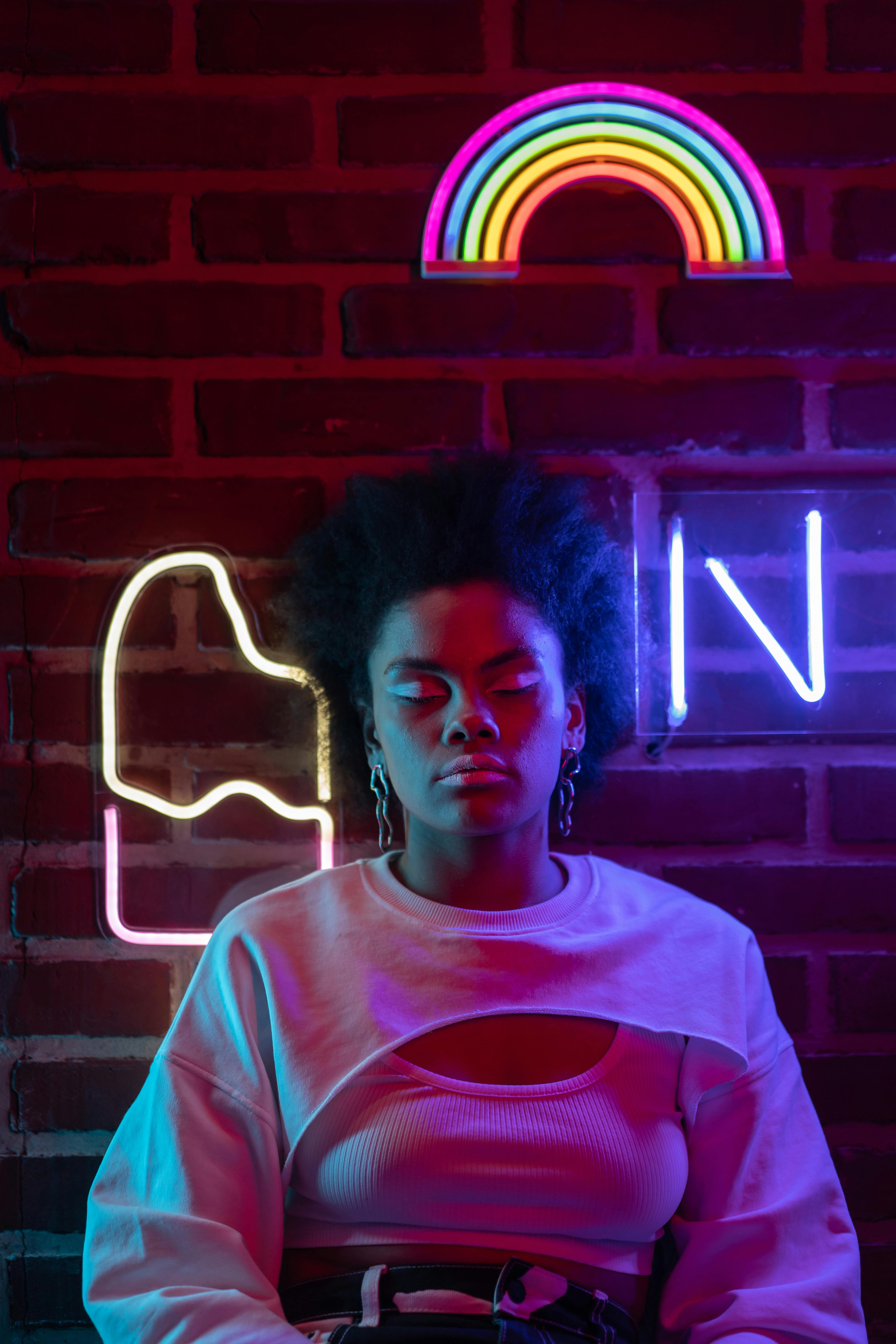 a woman in crop top long sleeve shirt sitting beside the brick wall with neon lights