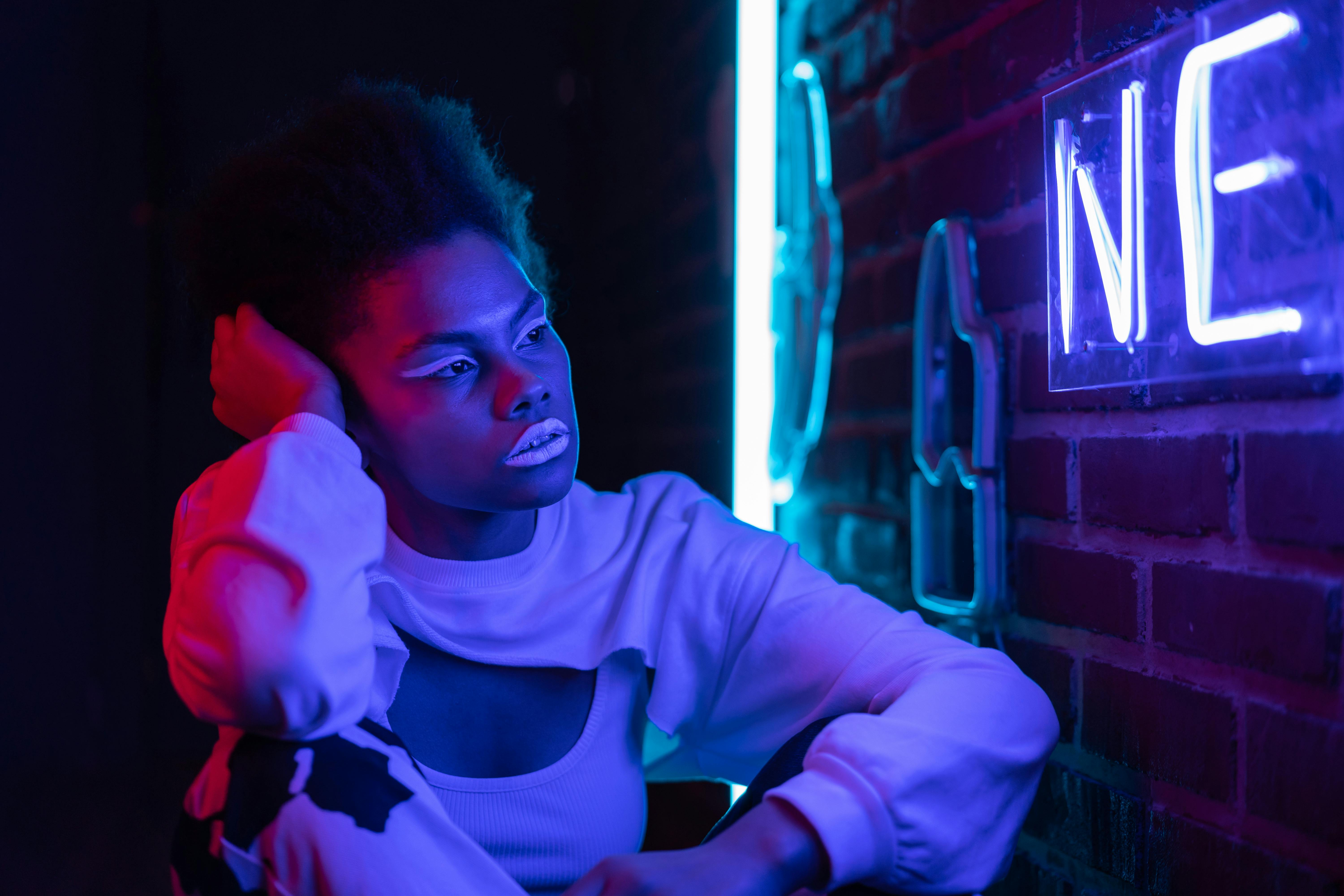 woman in white long sleeve shirt looking at the neon lights