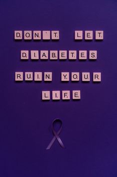 Motivating diabetes awareness message with scrabble tiles and ribbon on purple background.