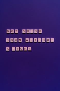 Motivational phrase 'Not going down without a fight' on a purple backdrop using Scrabble tiles.