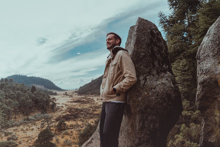 Man In Brown Jacket Leaning On Big Rock While Looking Afar