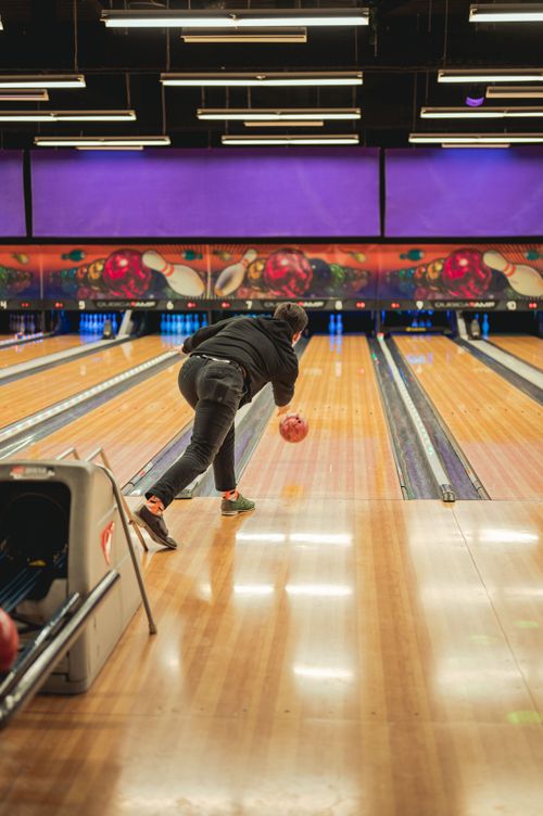 Free A man releases a bowling ball in a colorful indoor bowling alley, capturing the thrill of the sport. Stock Photo