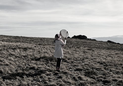 A person playing a buffalo drum in a vast, barren landscape.