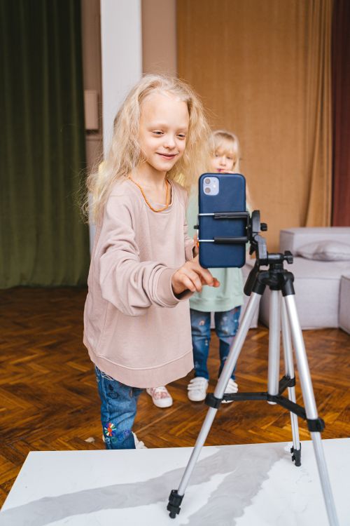 Free Two young girls recording with a smartphone on a tripod indoors, expressing creativity and enjoyment. Stock Photo