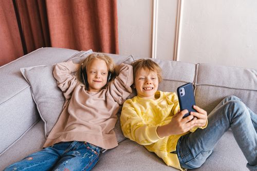 Free Two children laughing and posing for a selfie on a cozy couch, capturing a joyful moment of friendship and fun. Stock Photo