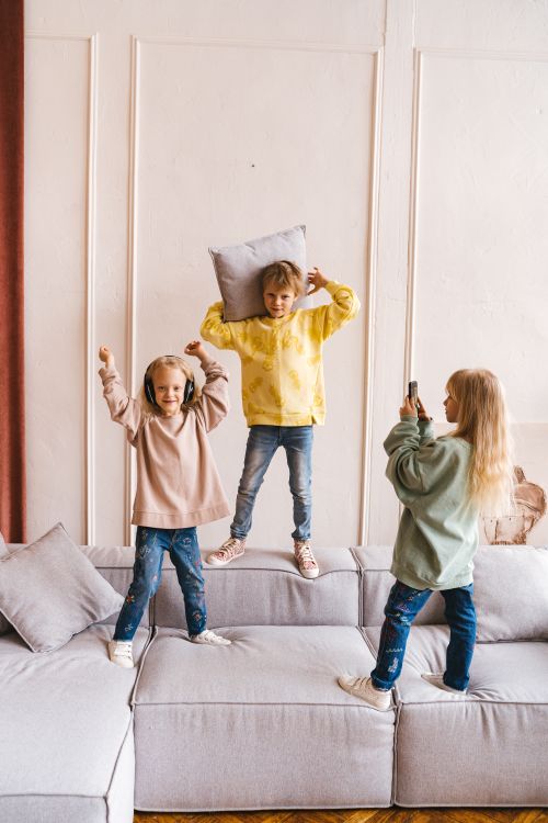 Free Three children having fun indoors with a pillow in a cozy setting. Stock Photo