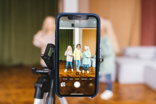 Free Three children record a video indoors using a smartphone on a tripod. Stock Photo