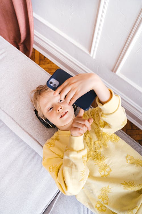 Boy using a Smartphone while lying on the Edge of Sofa