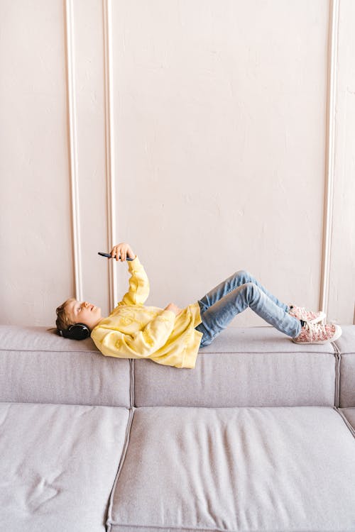 Boy using a Smartphone while lying on the Edge of Sofa