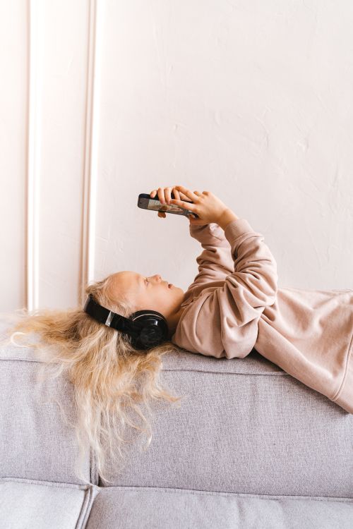 Free Child enjoying music and smartphone use at home, lying relaxed on a sofa. Stock Photo