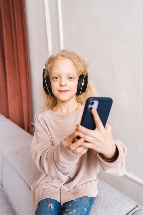 Free Blonde girl with headphones using smartphone indoors. Perfect for tech and lifestyle concepts. Stock Photo
