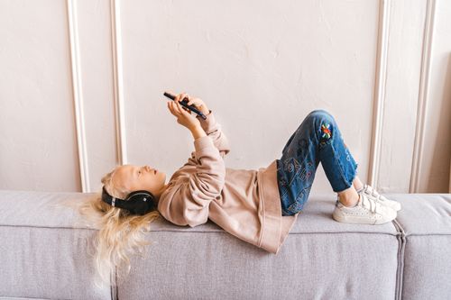 Free Young girl enjoying leisure time on sofa with headphones and smartphone indoors. Stock Photo