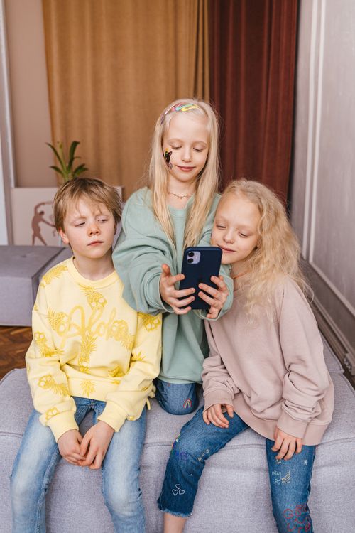 Free Three children sharing a moment with a smartphone indoors, embracing friendship and technology. Stock Photo