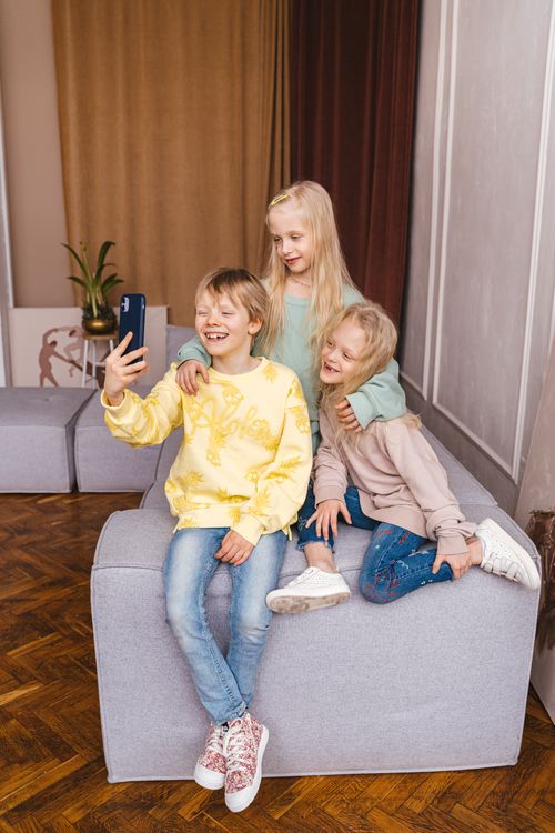 Free Three smiling children enjoy taking a selfie, capturing joyful memories and friendship indoors. Stock Photo