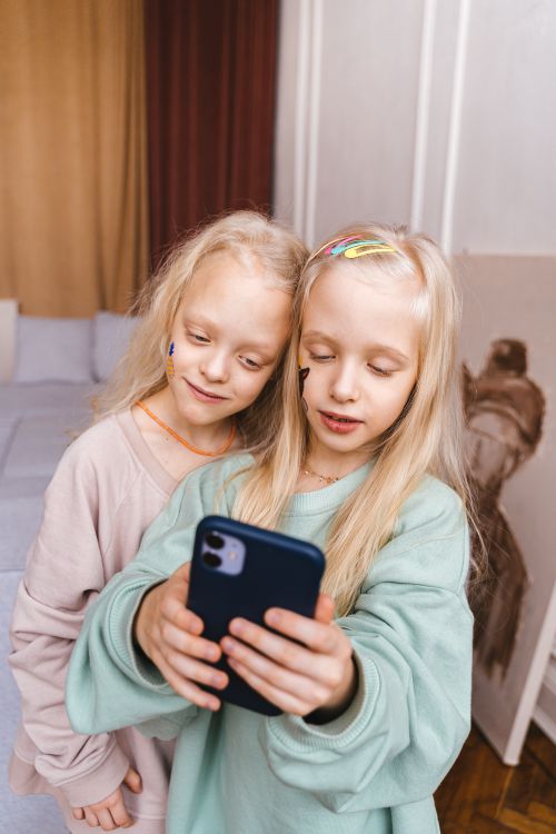 Free Two young girls enjoying a fun moment together by exploring a smartphone indoors. Stock Photo