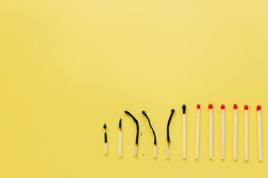 A row of burnt and unburnt matchsticks on a vibrant yellow background illustrating contrast.