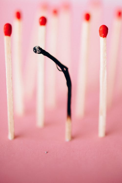Burnt Matchstick Surrounded by Unburn Matchsticks on a Pink Surface