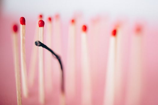 A burned matchstick in focus symbolizing burnout, surrounded by unlit matchsticks on a pink background.