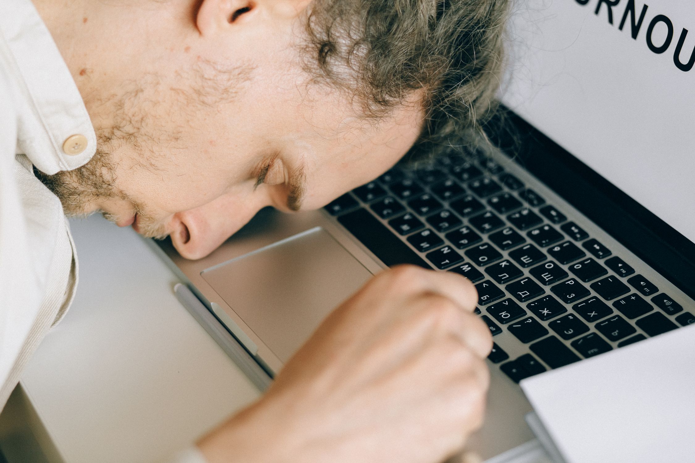Pessoa exausta no ambiente de trabalho com as mãos no rosto, simbolizando o esgotamento mental e a falta de descanso adequado.