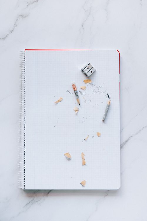 Free Overhead view of a spiral notebook with pencils, shavings, and a sharpener on a marble surface. Stock Photo