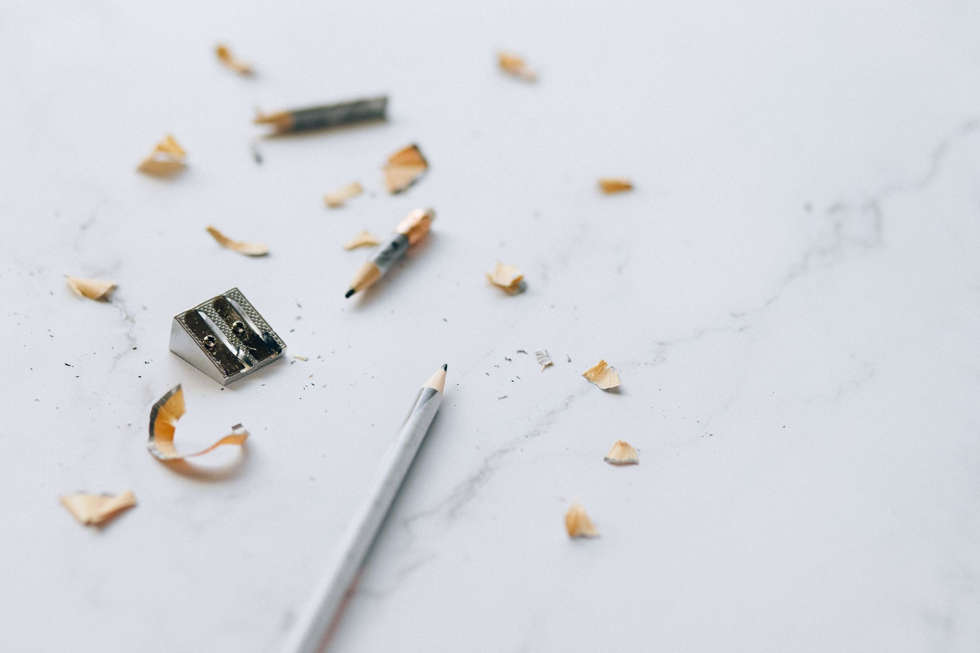 Close-up of pencil, sharpener, and shavings on a marble surface for artistic effect.