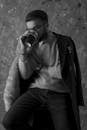 Grayscale Photo of a Man Wearing Coat Drinking on a Glass