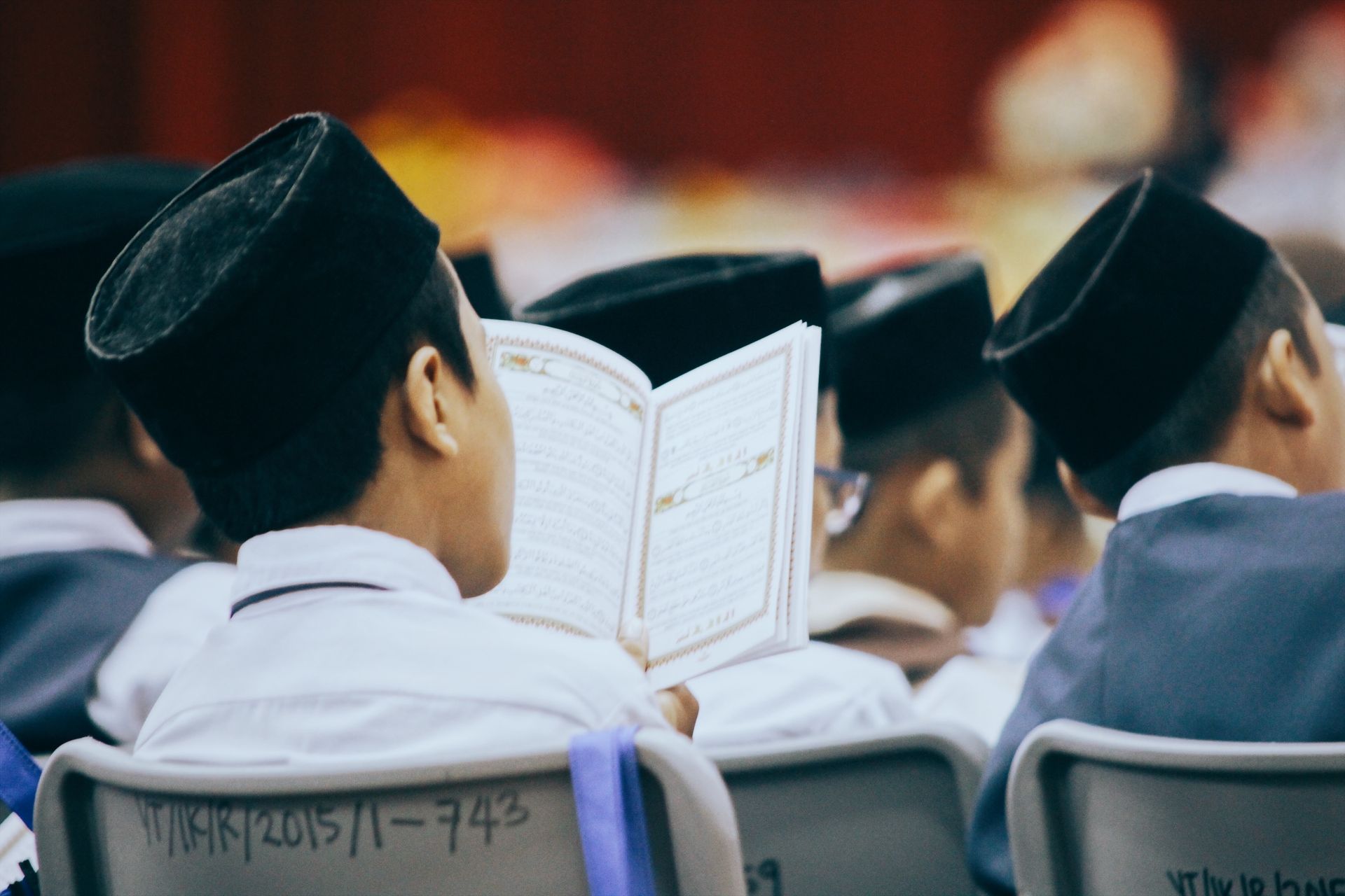 Boys in traditional attire reading the Quran during a religious gathering, showcasing faith and devotion.