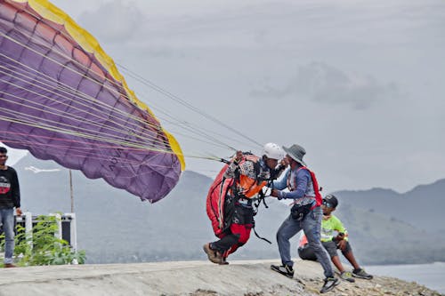 2 Men in Red Jacket and Blue Denim Jeans Holding Yellow Blue and Red Parachute