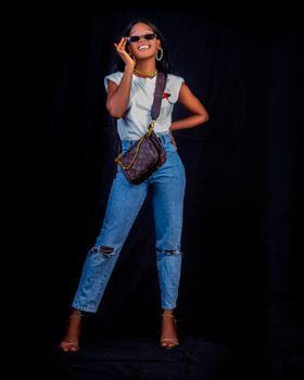Fashionable woman poses confidently in sunglasses and denim, smiling in a studio setting.