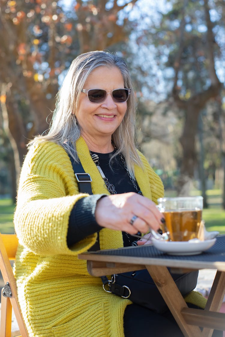 An Elderly Woman Sitting At The Park While Holding A Cup Of Tea