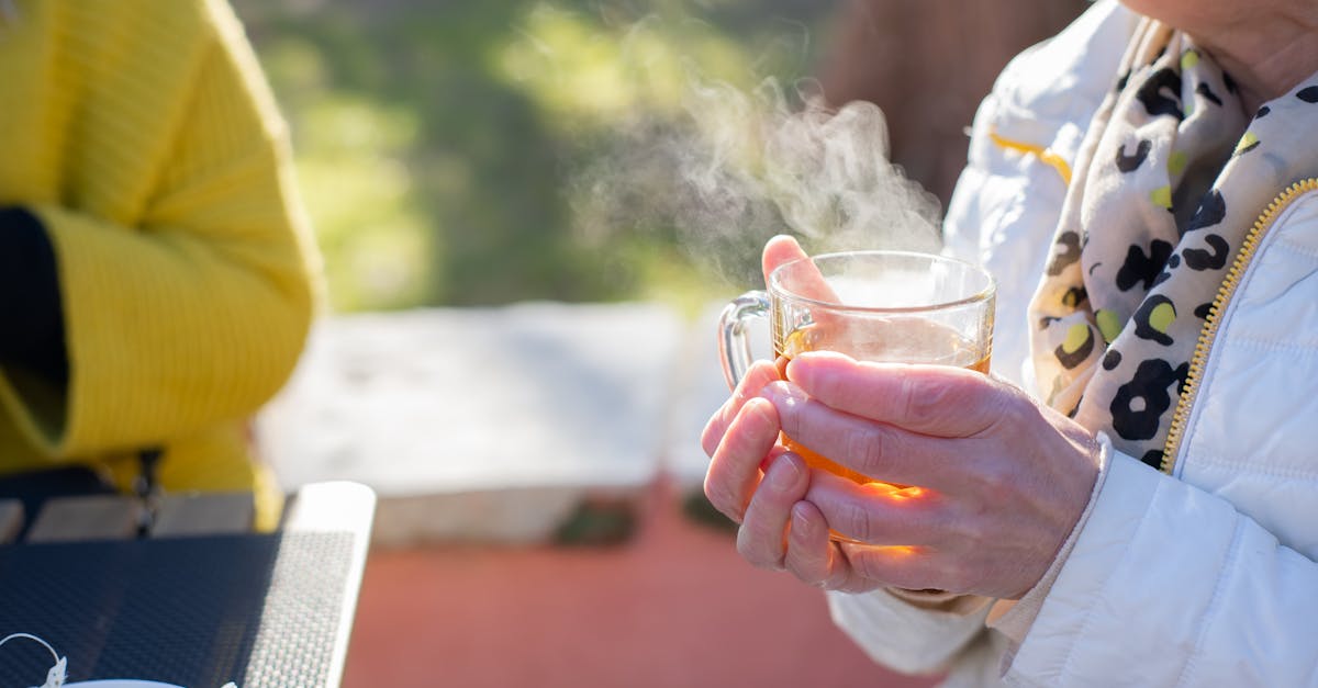 Elderly woman savoring hot tea outdoors, capturing warmth and relaxation in natural setting.