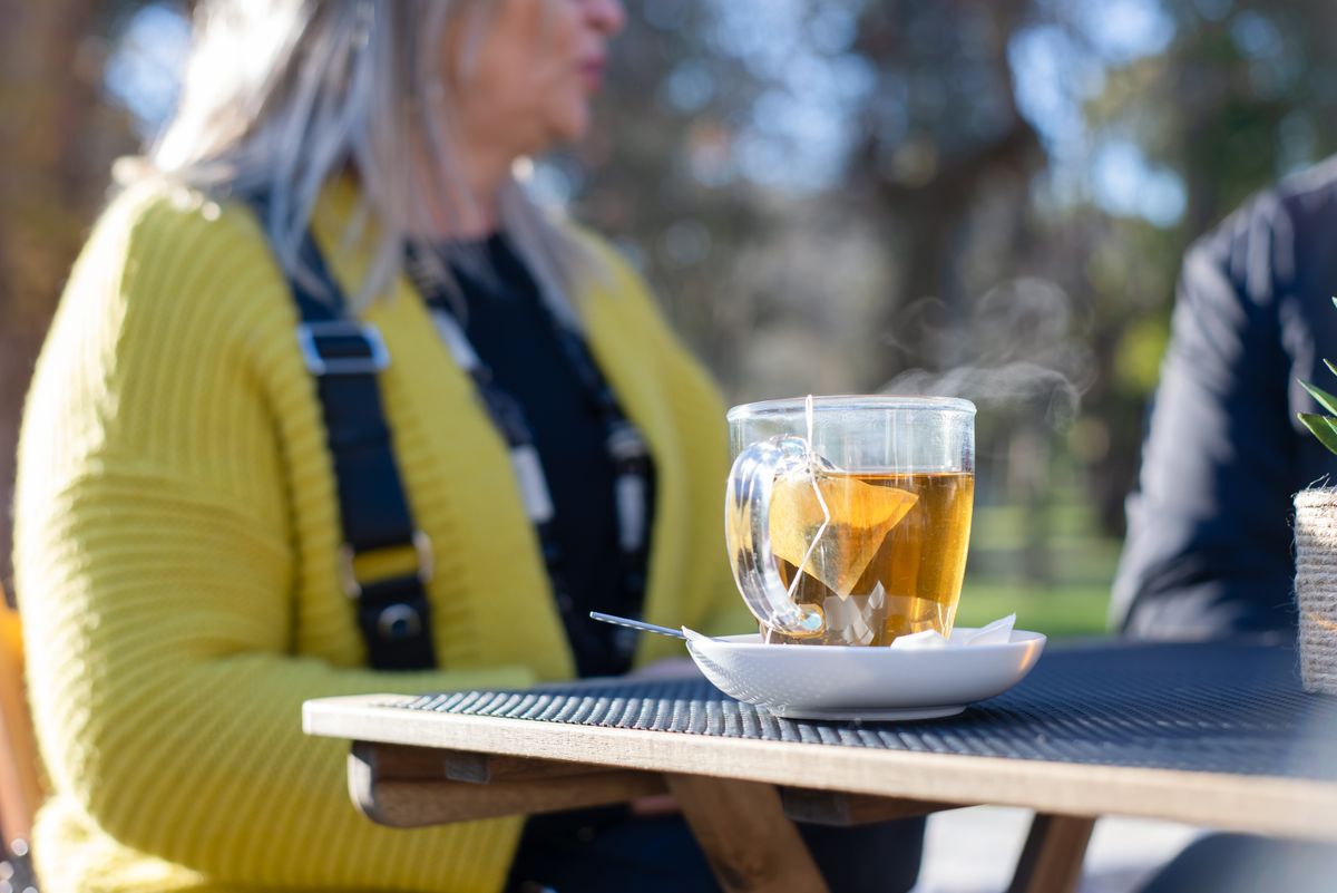 Woman in her 40s relaxing outdoors while drinking a warm cup of tea