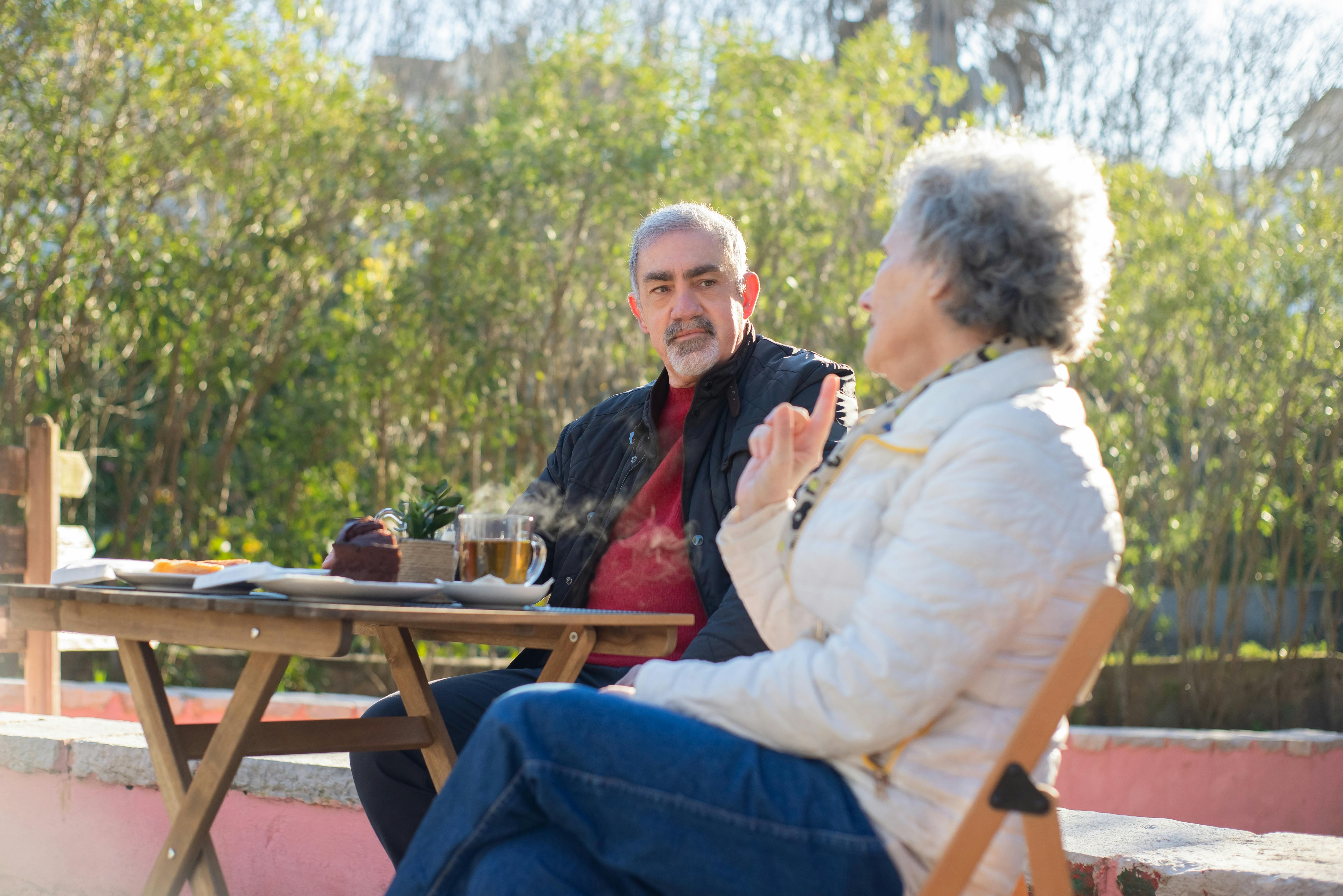 Elderly couple enjoying a relaxed coffee break outdoors on a sunny day.