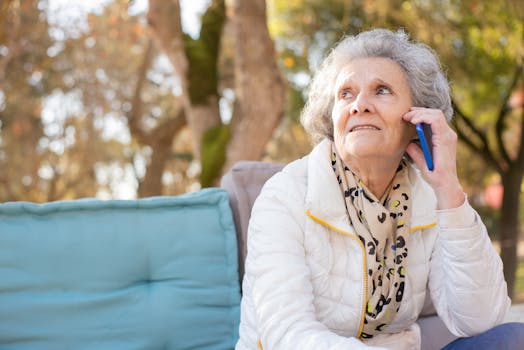 Senior woman in white jacket having a phone conversation in an outdoor park setting.