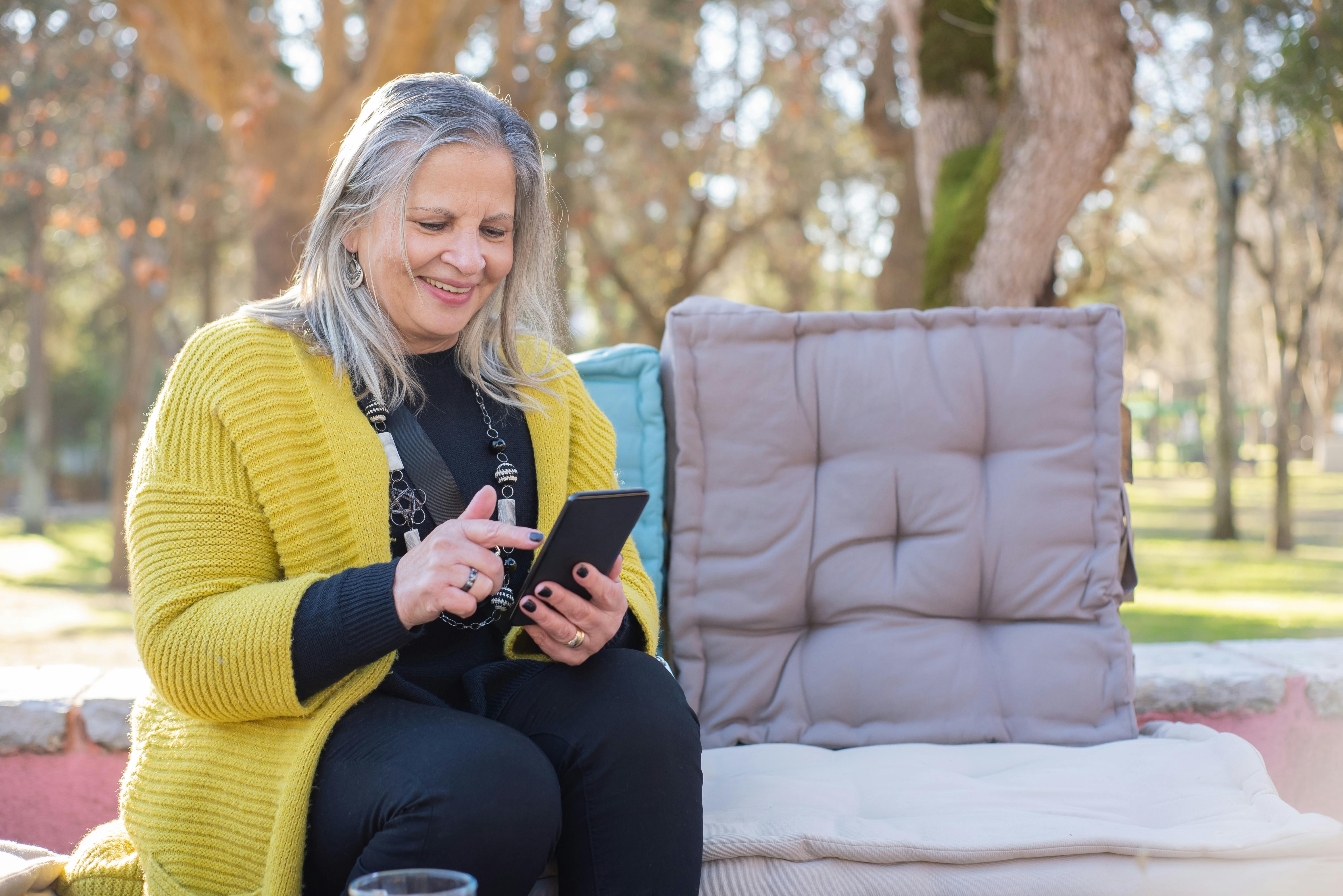 an elderly woman in yellow cardigan smiling while using her mobile phone