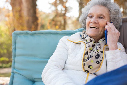 Smiling senior woman talking on cellphone outdoors in a park setting, enjoying a cheerful phone call.