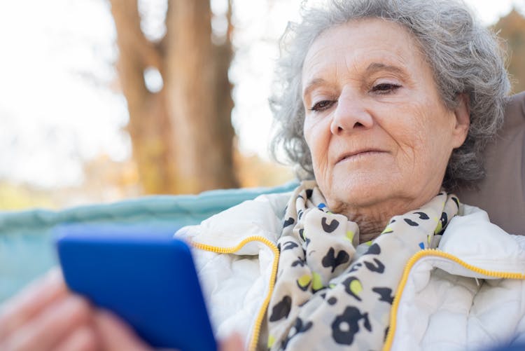 An Elderly Woman In White Jacket Using Her Mobile Phone