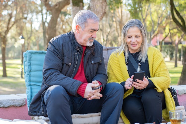 An Elderly Man And Woman Sitting At The Park While Having Conversation