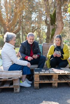 A group of senior adults playing cards together outdoors, enjoying leisure time on a sunny day.