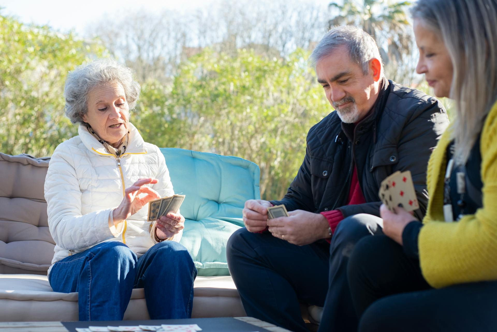 Elderly friends playing cards together outdoors on a sunny day, enjoying leisure time in Portugal.