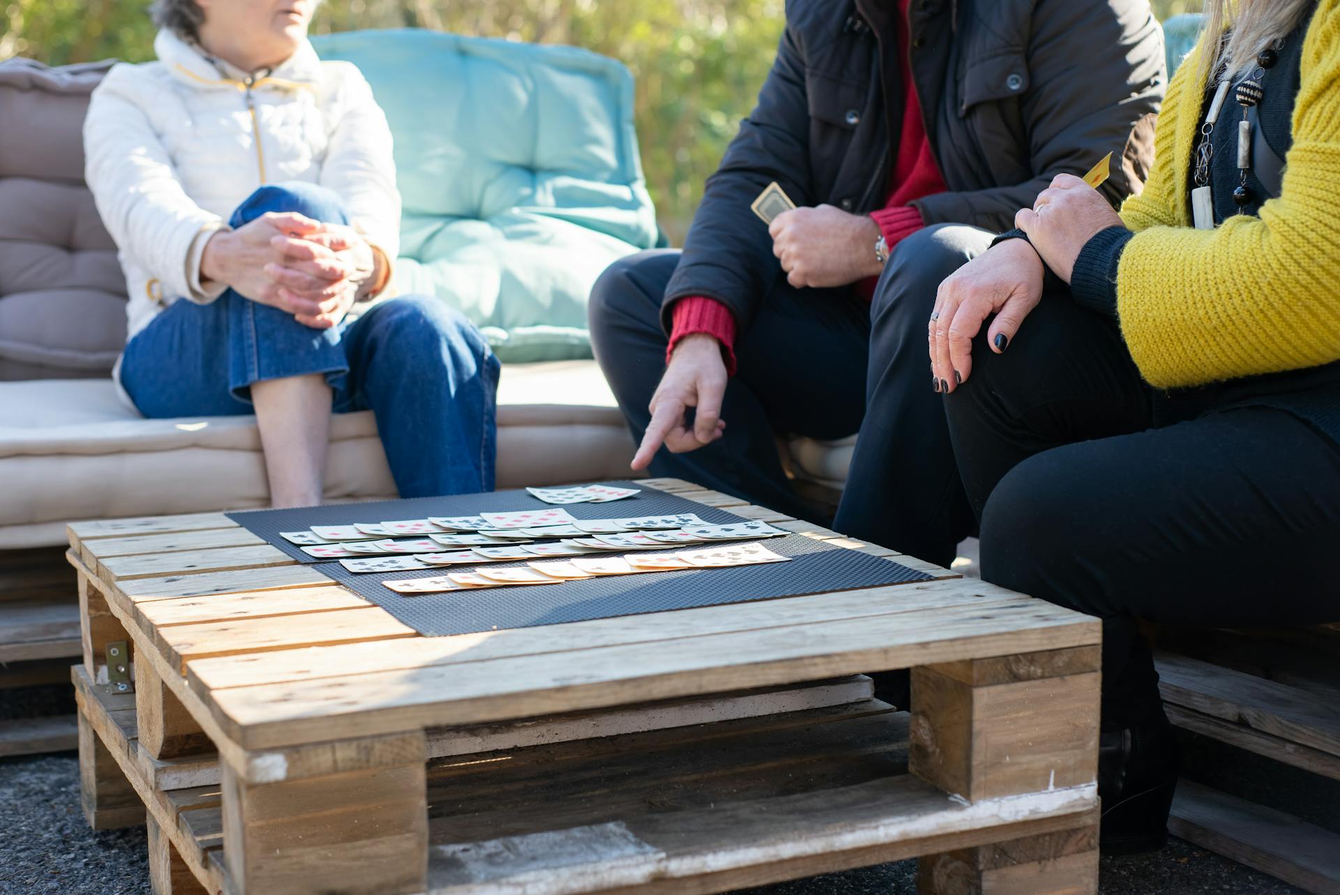 A group of adults playing solitaire on a wooden table outdoors.