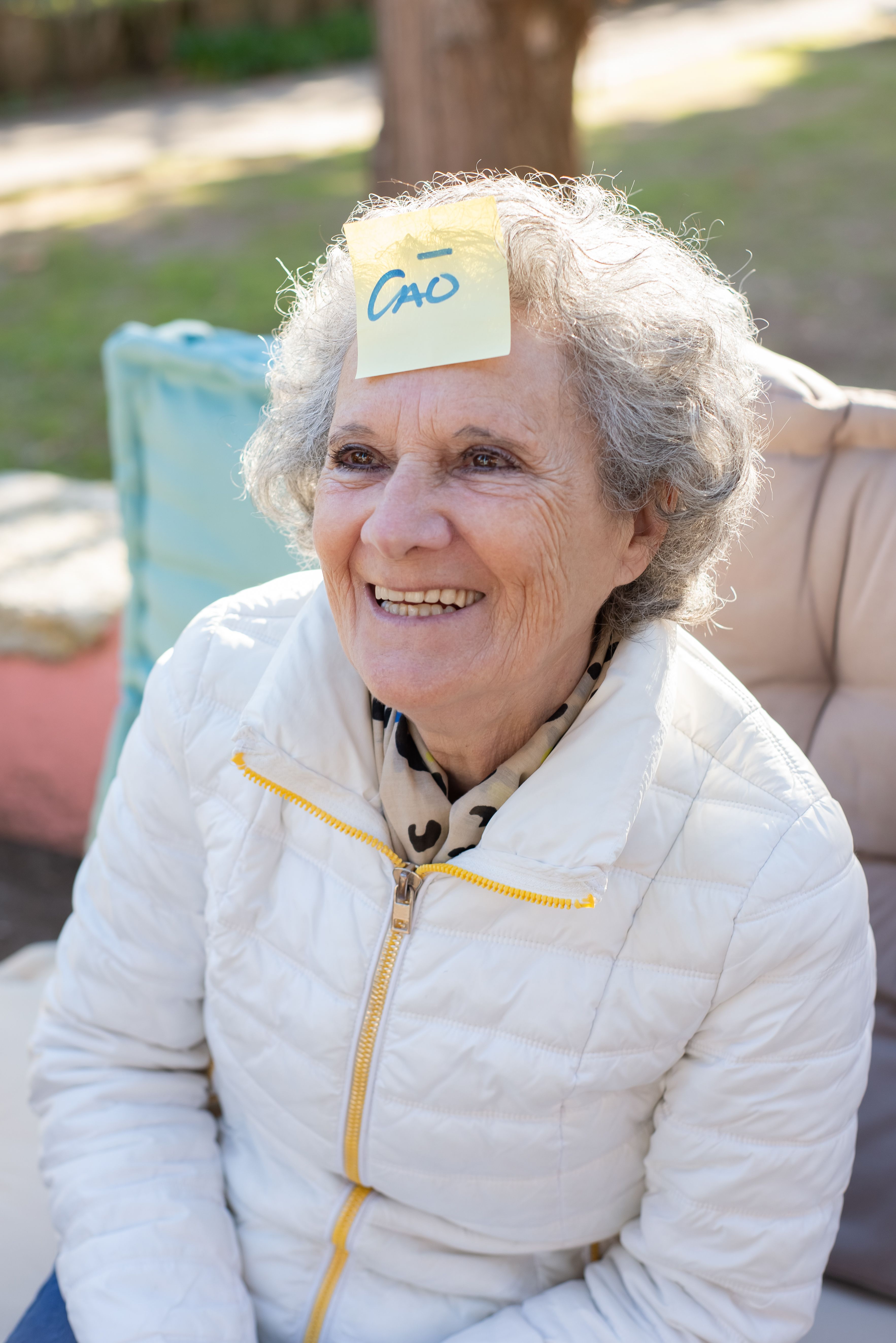 Happy elderly woman with a sticky note on her forehead enjoys a sunny day outside.