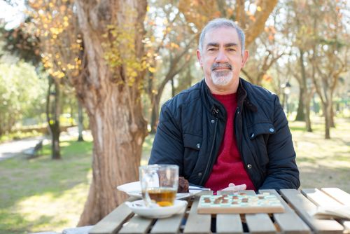 Free Senior man smiling while enjoying a board game in a sunny park setting, embodying positive aging. Stock Photo