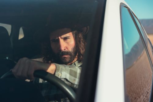 Free A rugged bearded man with a cowboy hat driving a car on a sunny road trip. Stock Photo