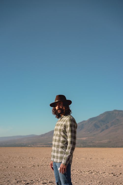 Free Man in plaid shirt and fedora exploring a barren desert landscape. Stock Photo